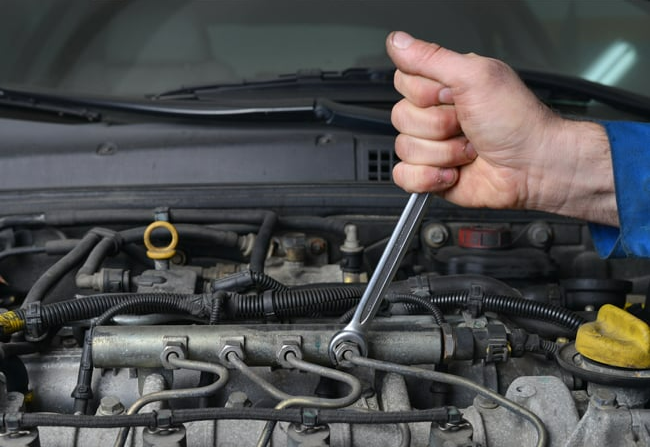 A person is working on a car engine with a wrench.