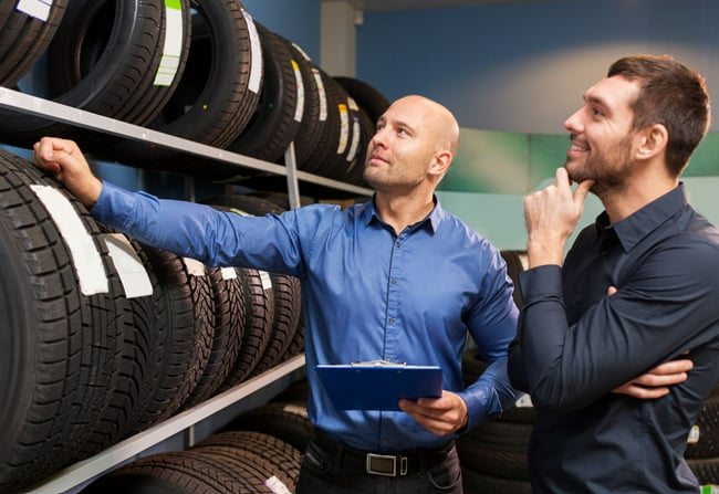 Two men are looking at tires in a tire store.