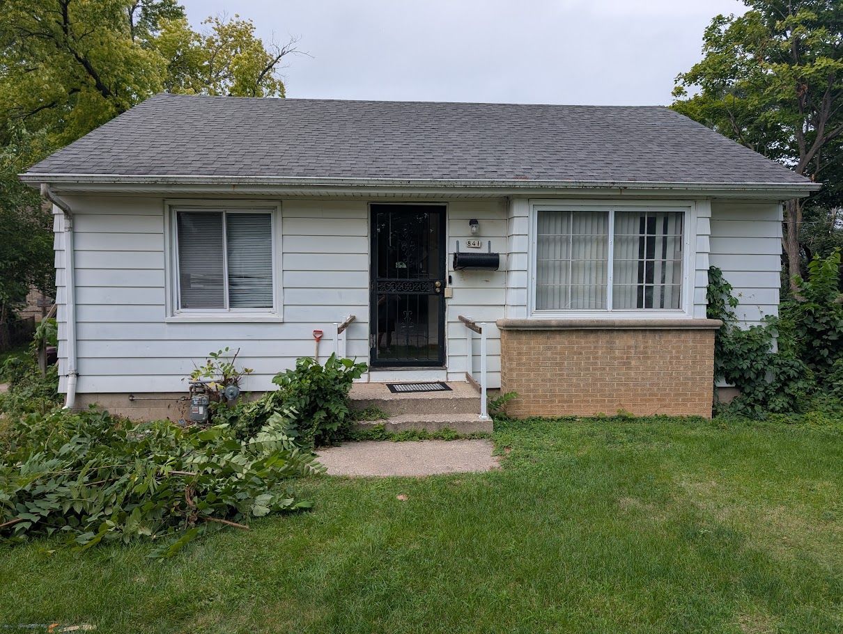 Small white single-story house with a dark roof, front porch, and green lawn.