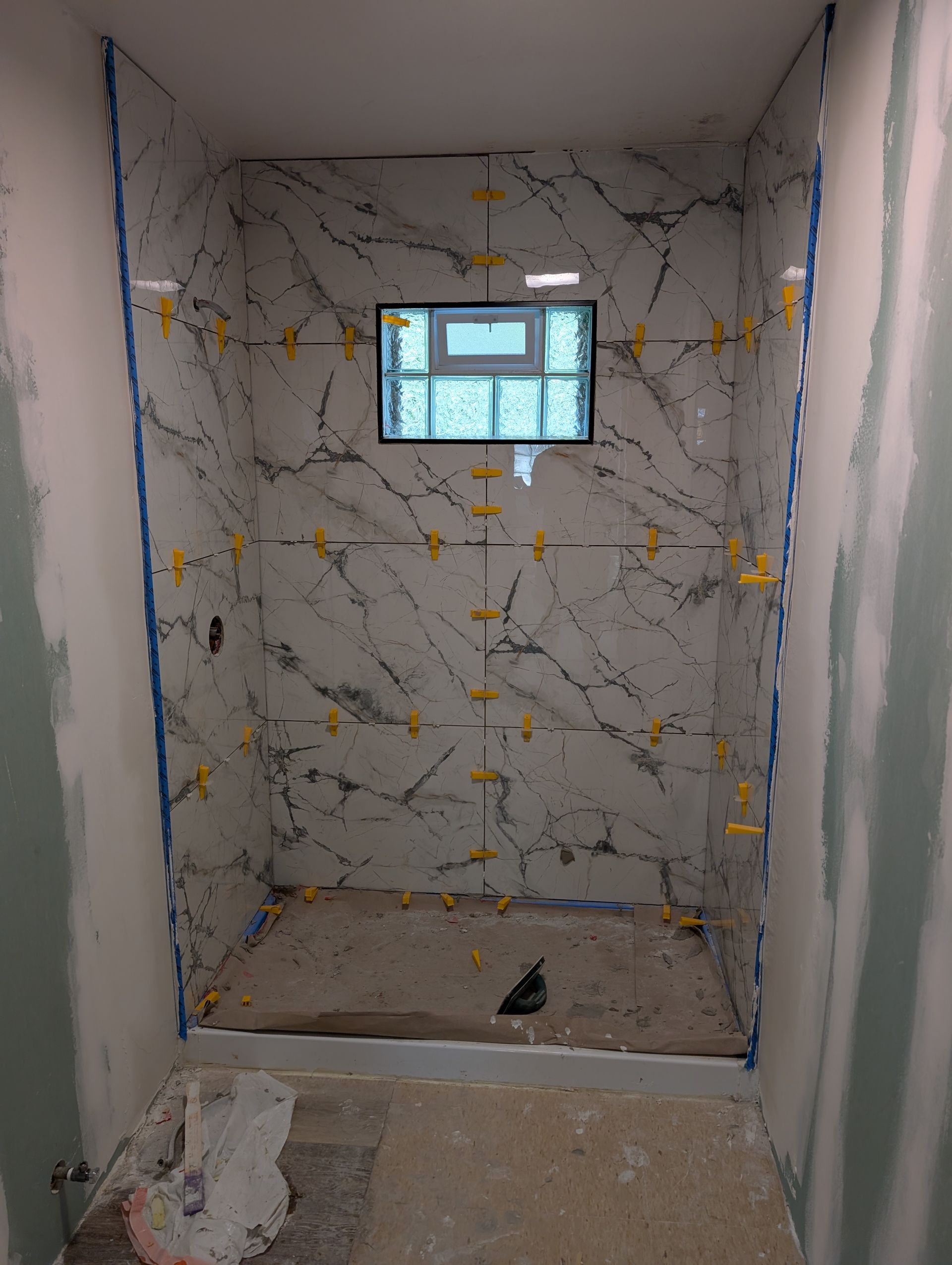 Small tiled shower stall under construction with a tiny window and unfinished floor drain opening.