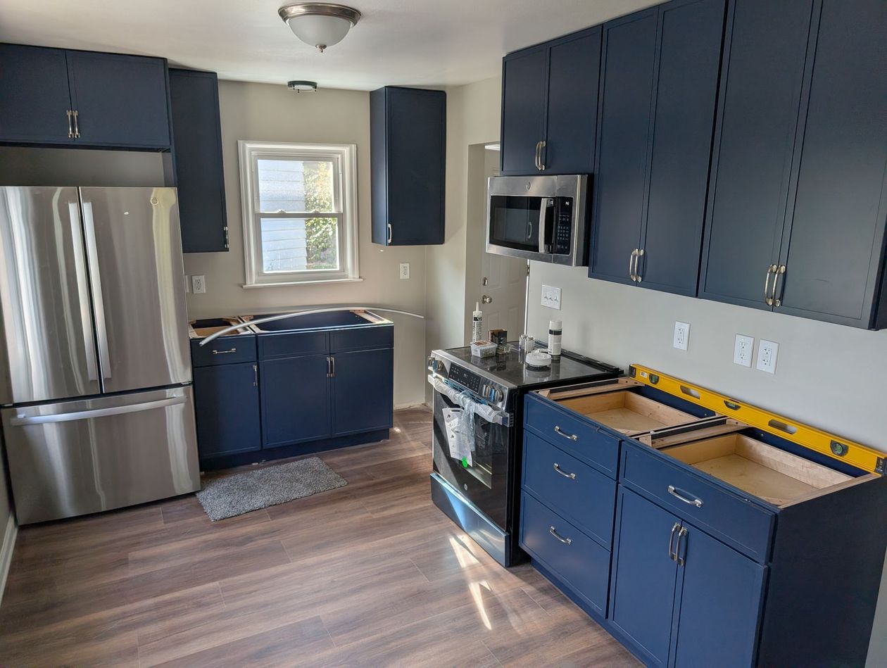 Blue kitchen with stainless steel appliances, window over the sink, and wood-look flooring