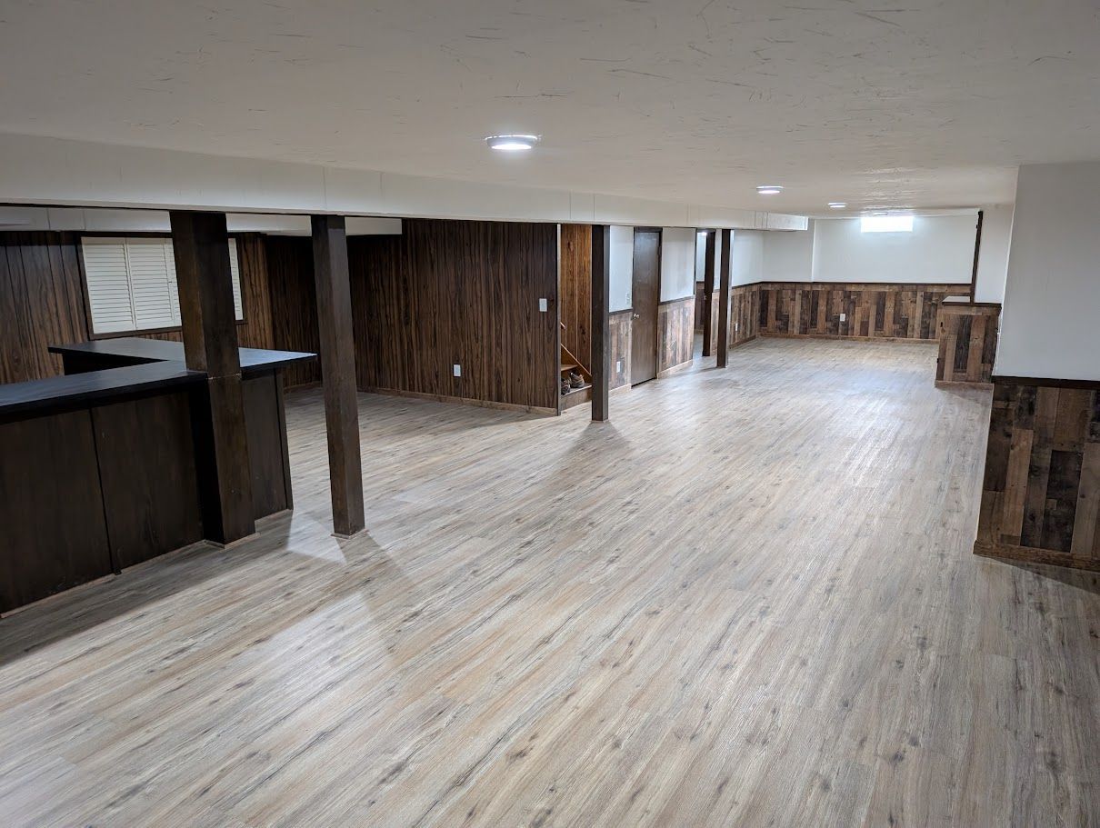 Empty wood-paneled basement room with light wood flooring and a low ceiling