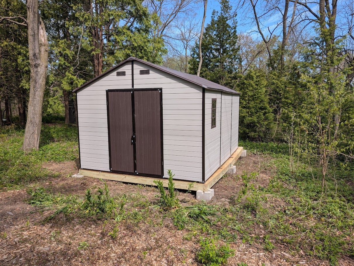 Small white garden shed with dark doors in a wooded clearing