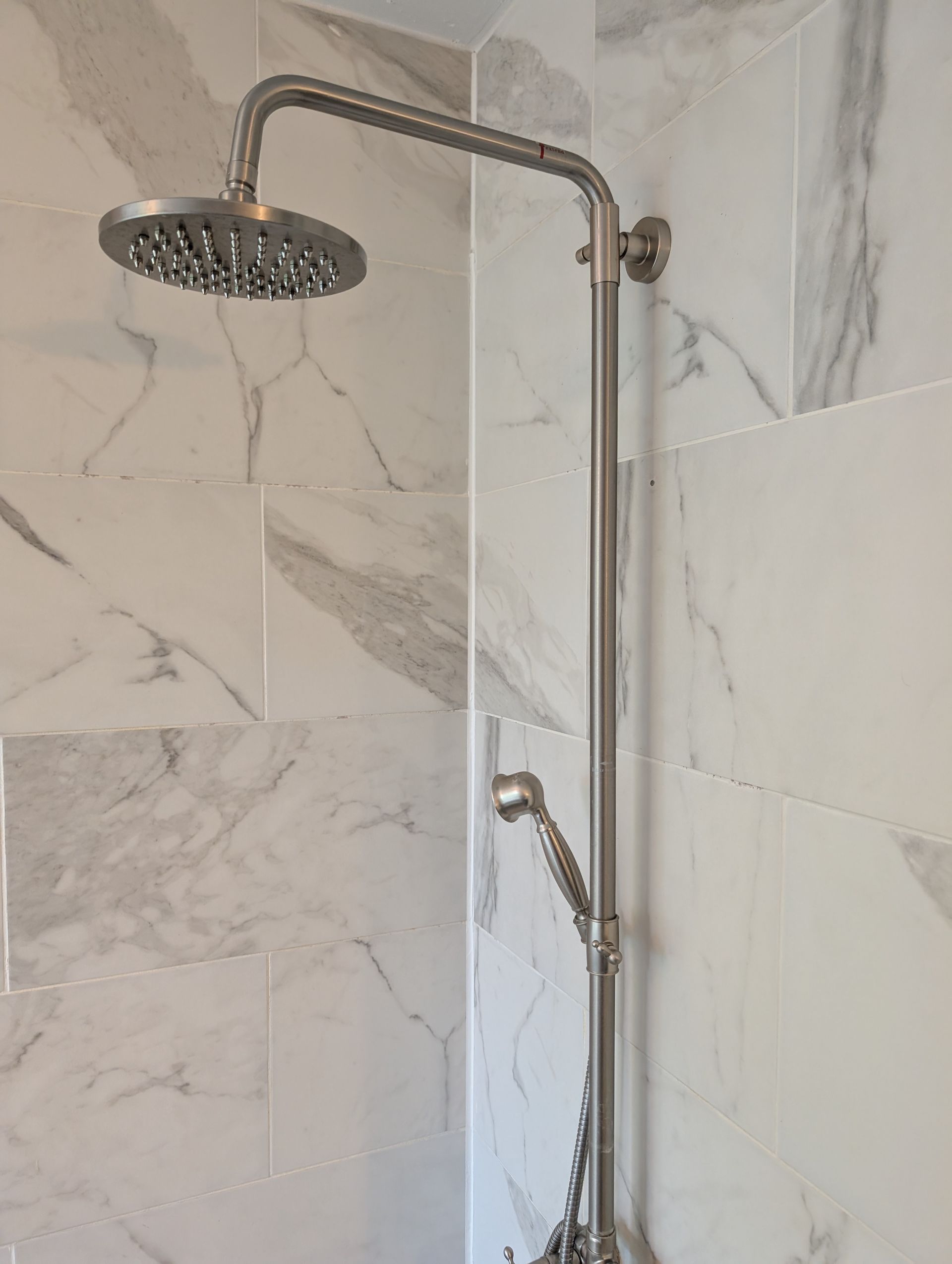 Round shower head and vertical grab bar against white marble-tile bathroom wall