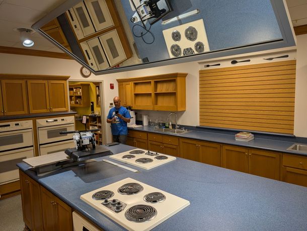Kitchen with blue countertops, wooden cabinets, and a person cleaning near the back wall. Kitchen with blue countertops, wooden cabinets, and a person cleaning near the back wall.