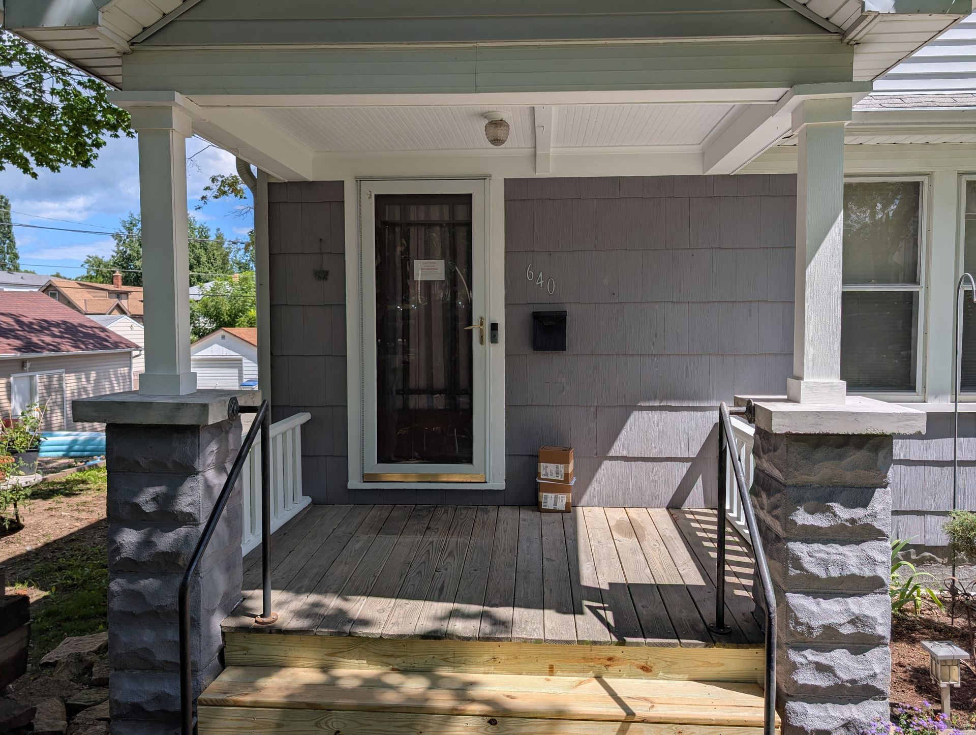 Front porch with white door, gray siding, and stone pillars under a covered roof Front porch with white door, gray siding, and stone pillars under a covered roof