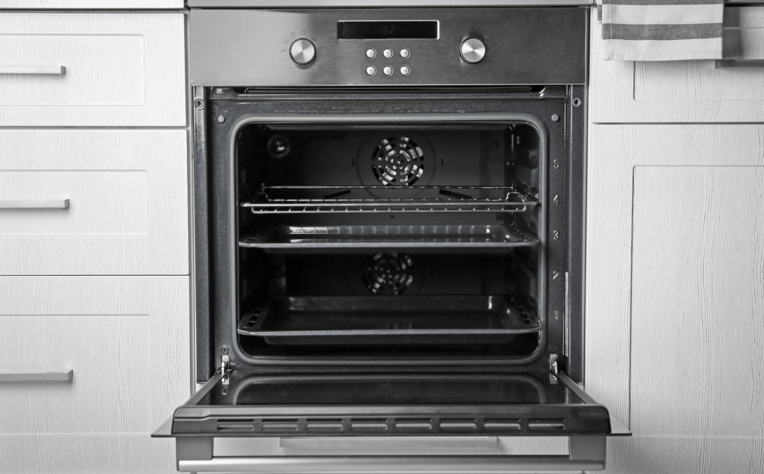 Open oven in a modern kitchen, with metal racks and control panel visible.