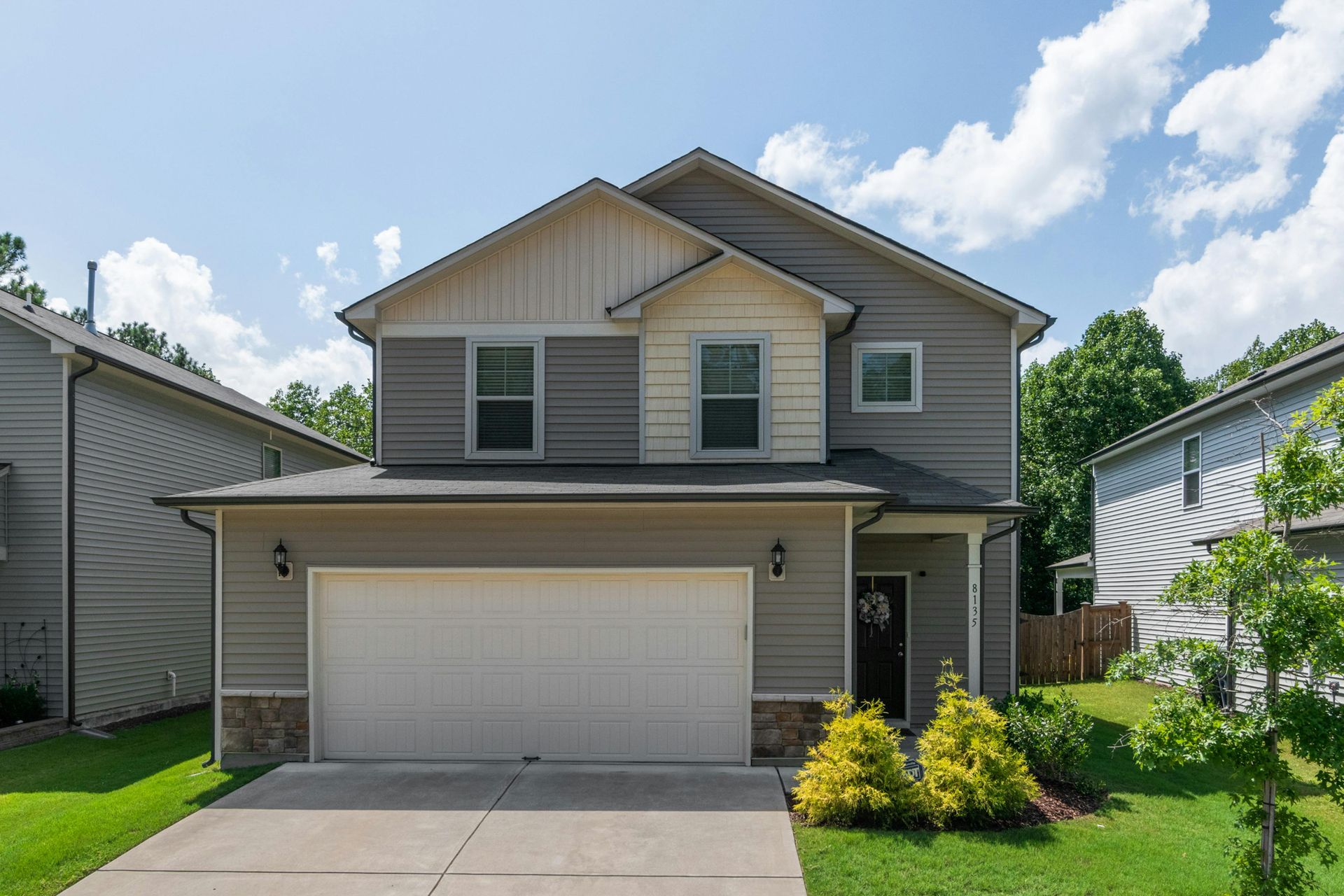 Two-story beige suburban house with a two-car garage and green lawn under a sunny sky