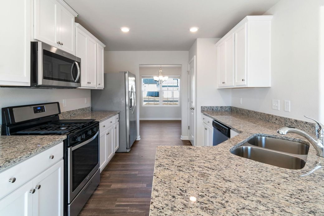 Bright modern kitchen with white cabinets, granite counters, stainless appliances, and dark wood floors