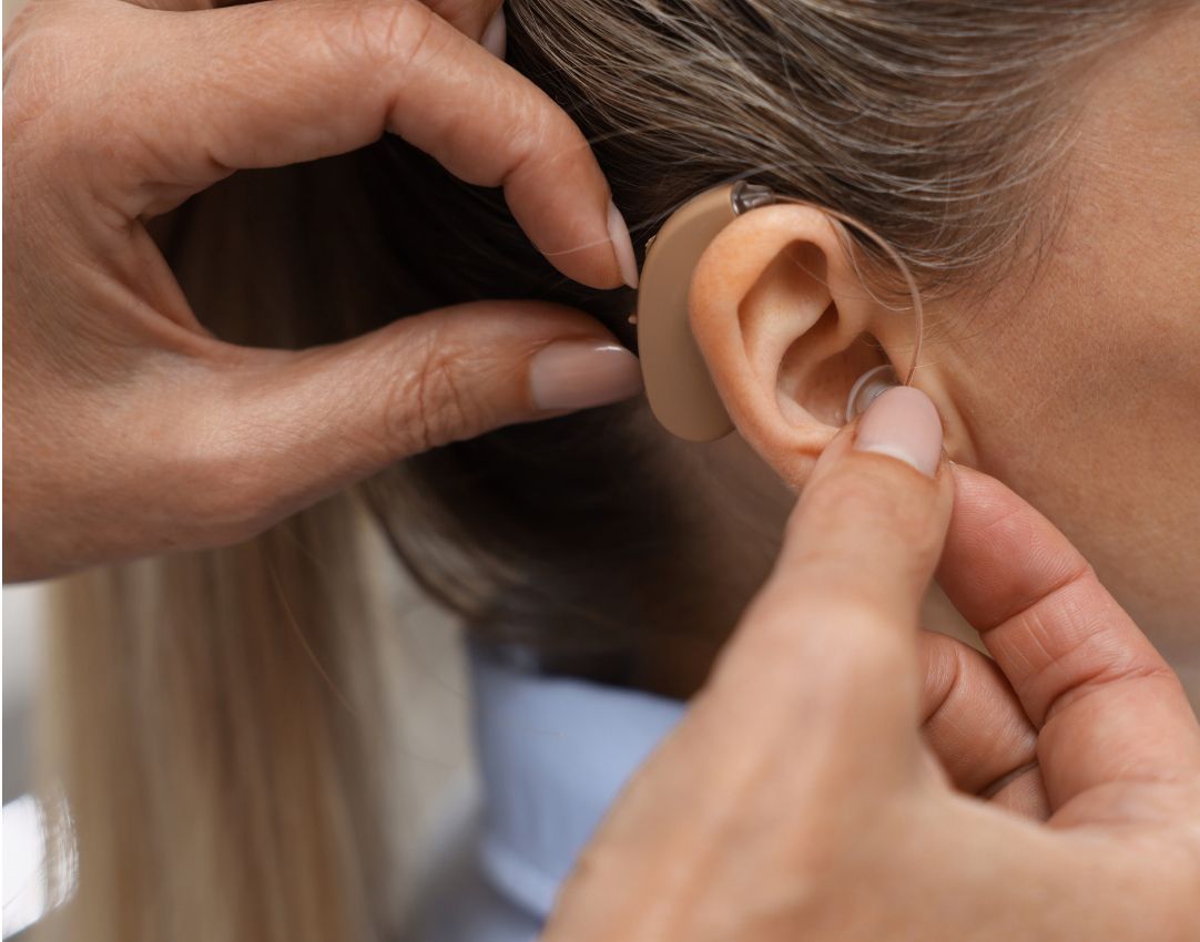 Clinician fitting a behind-the-ear hearing aid and ear dome on a woman's ear