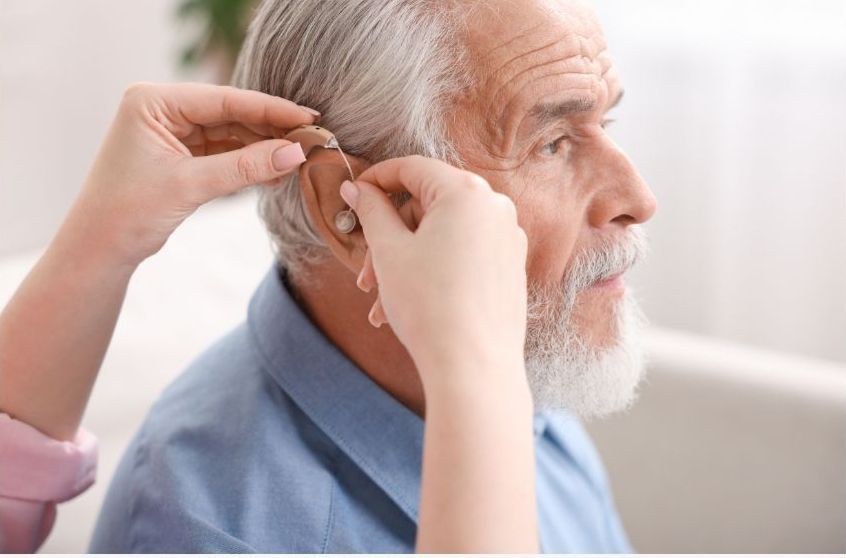 Audiologist fitting a behind-the-ear hearing aid on an older man during a professional hearing test.