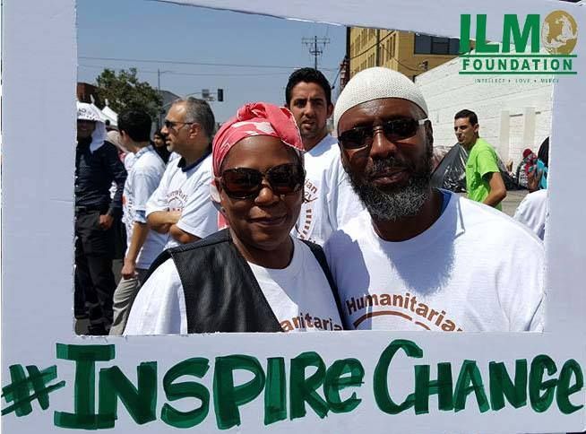 Two people framed in a sign, smiling, wearing white shirts. Crowd in background, text reads: Inspire Change.