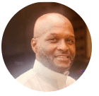 Smiling Black man with a shaved head and beard, wearing a white collared shirt.