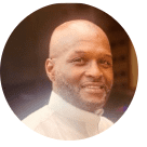 Smiling Black man with a shaved head, wearing a white collared shirt.