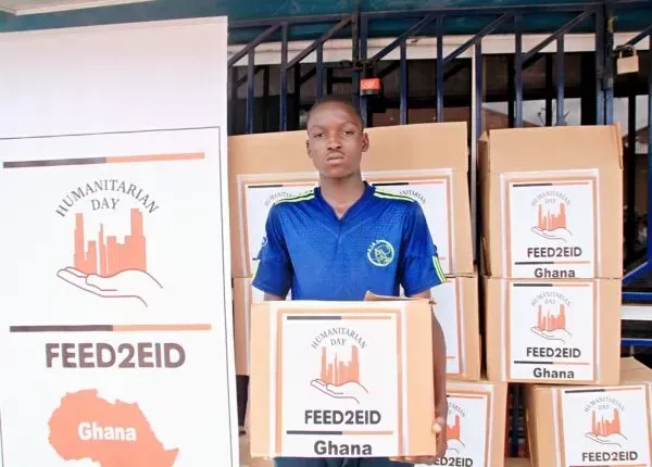 A person stands holding a box, in front of boxes with