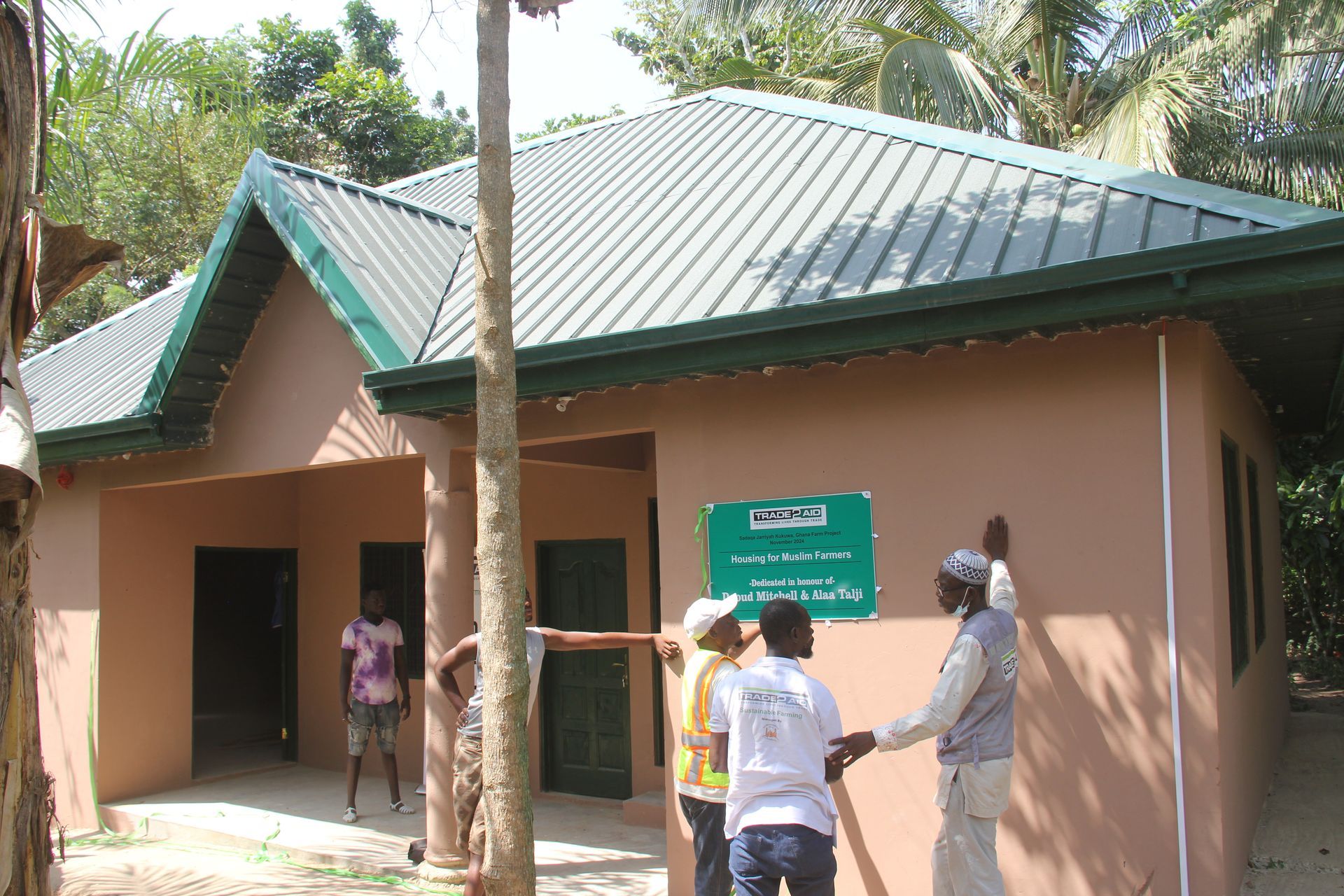 A group of people standing in front of a house with a green sign on the wall