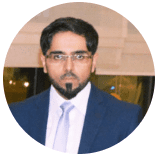 Man in a suit and tie with a goatee, wearing glasses, possibly in a formal setting.