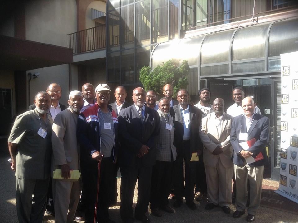 Group of men in business attire pose outside a building.