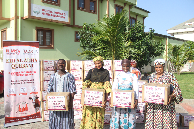 People holding boxes for Eid al-Adha in front of a building. Boxes are labeled 