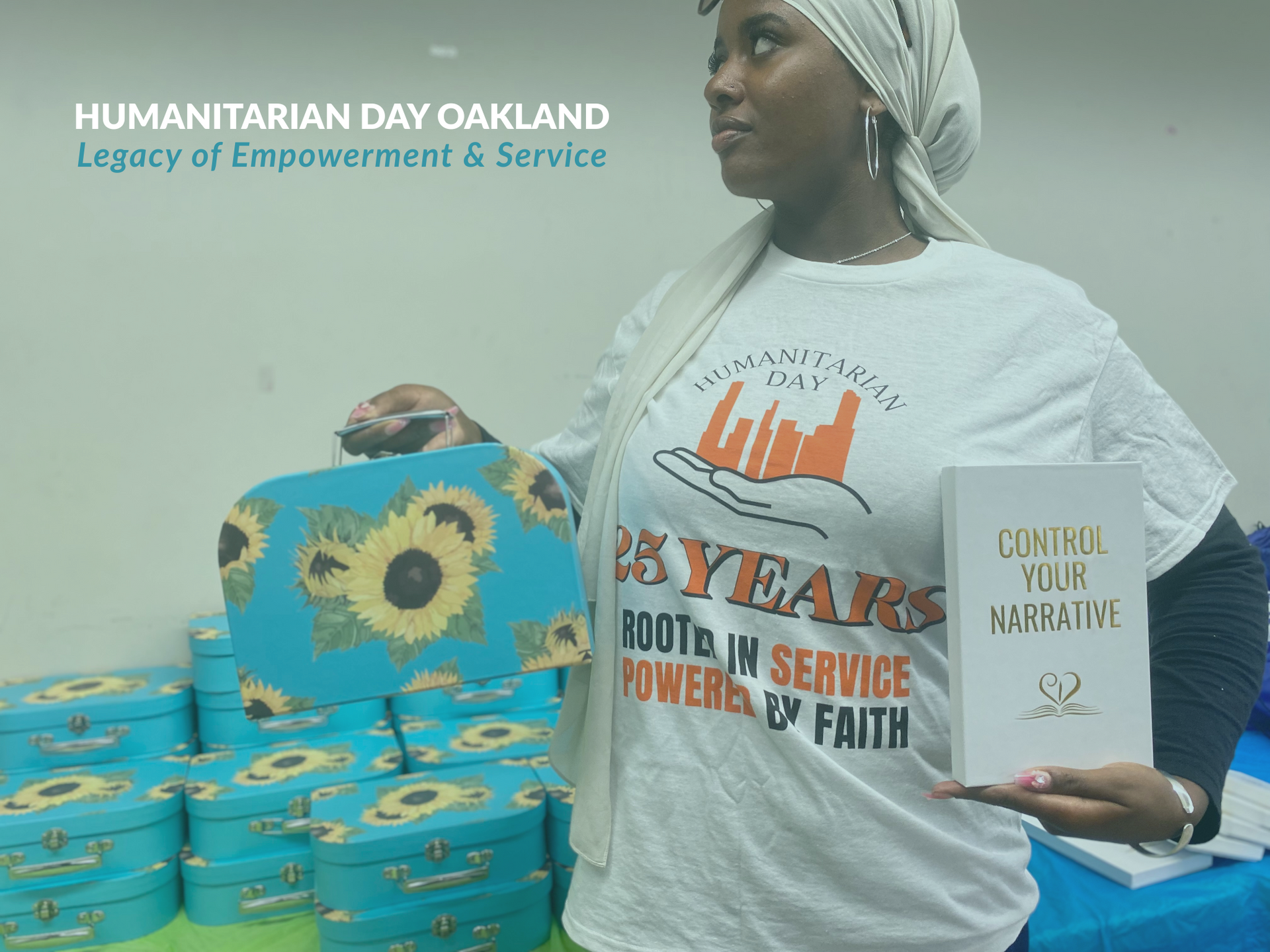 Woman holding a purse and book, near stacked boxes. Humanitarian Day Oakland logo on shirt. Text: 