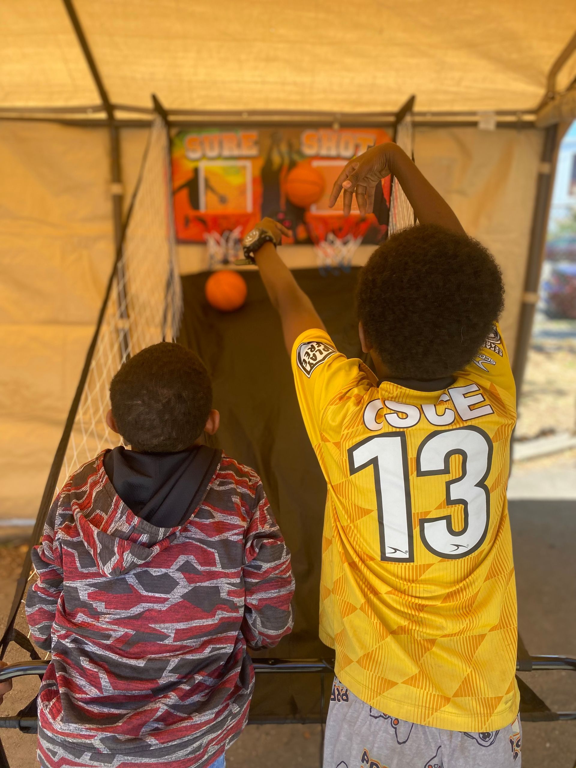 Two people playing basketball arcade game outdoors.