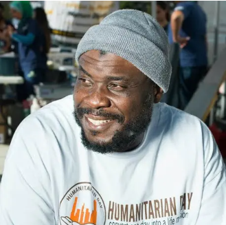 Man in gray beanie and Humanitarian Day shirt smiles outdoors.