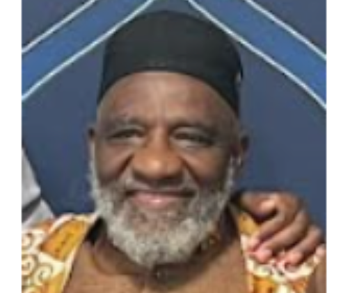 Older Black man with a gray beard and black cap, smiling. He wears a patterned garment.