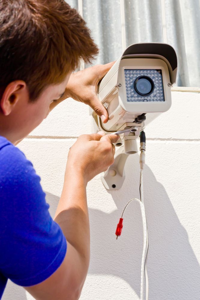 A Man is Fixing a Security Camera on a Wall — Cambush Security Solutions NT in Katherine, NT