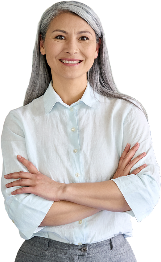 Woman with gray hair smiles, arms crossed, wearing a light blue button-down shirt and gray pants.