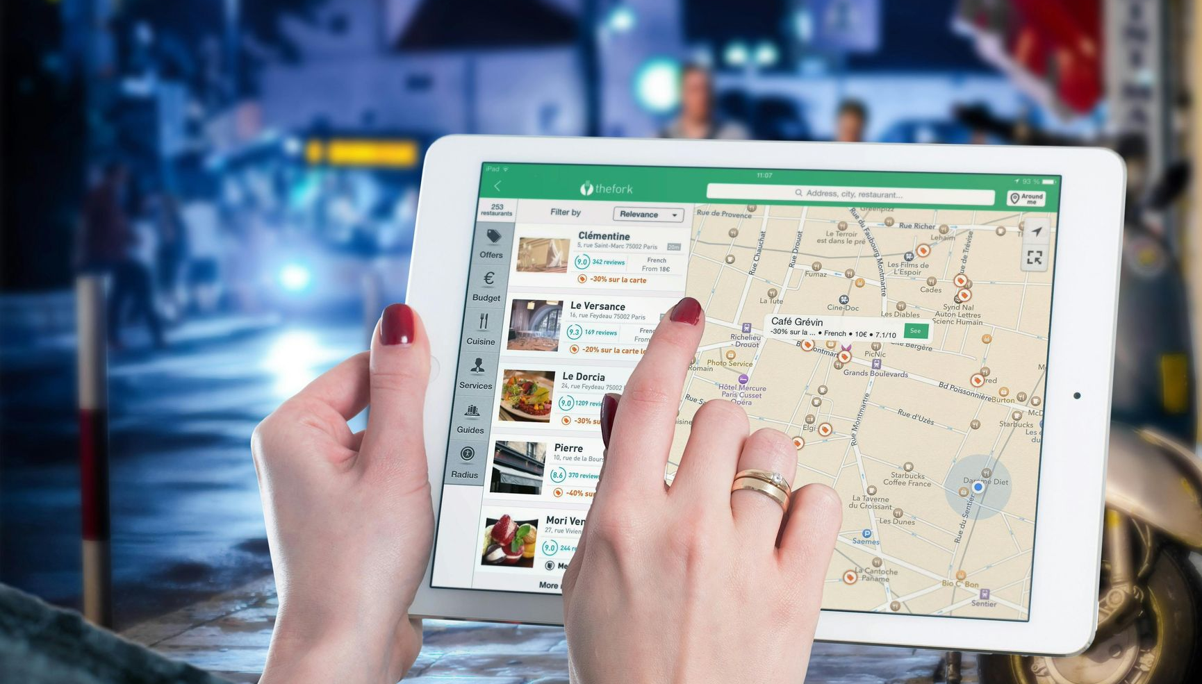 Hands holding a tablet displaying a map and food listing, outdoors at night.