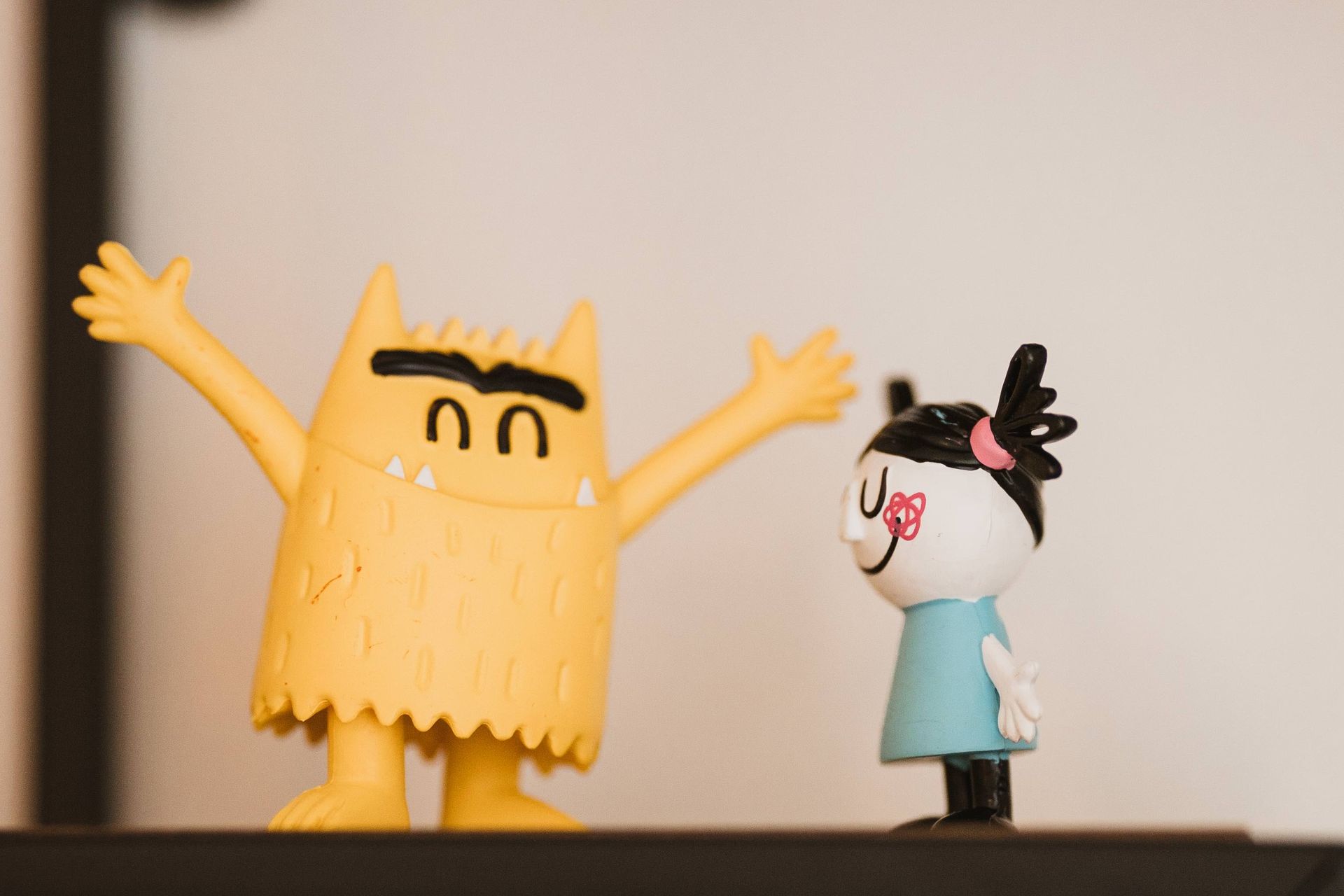 Monstre jaune les bras levés et une figurine de fille qui le regarde.