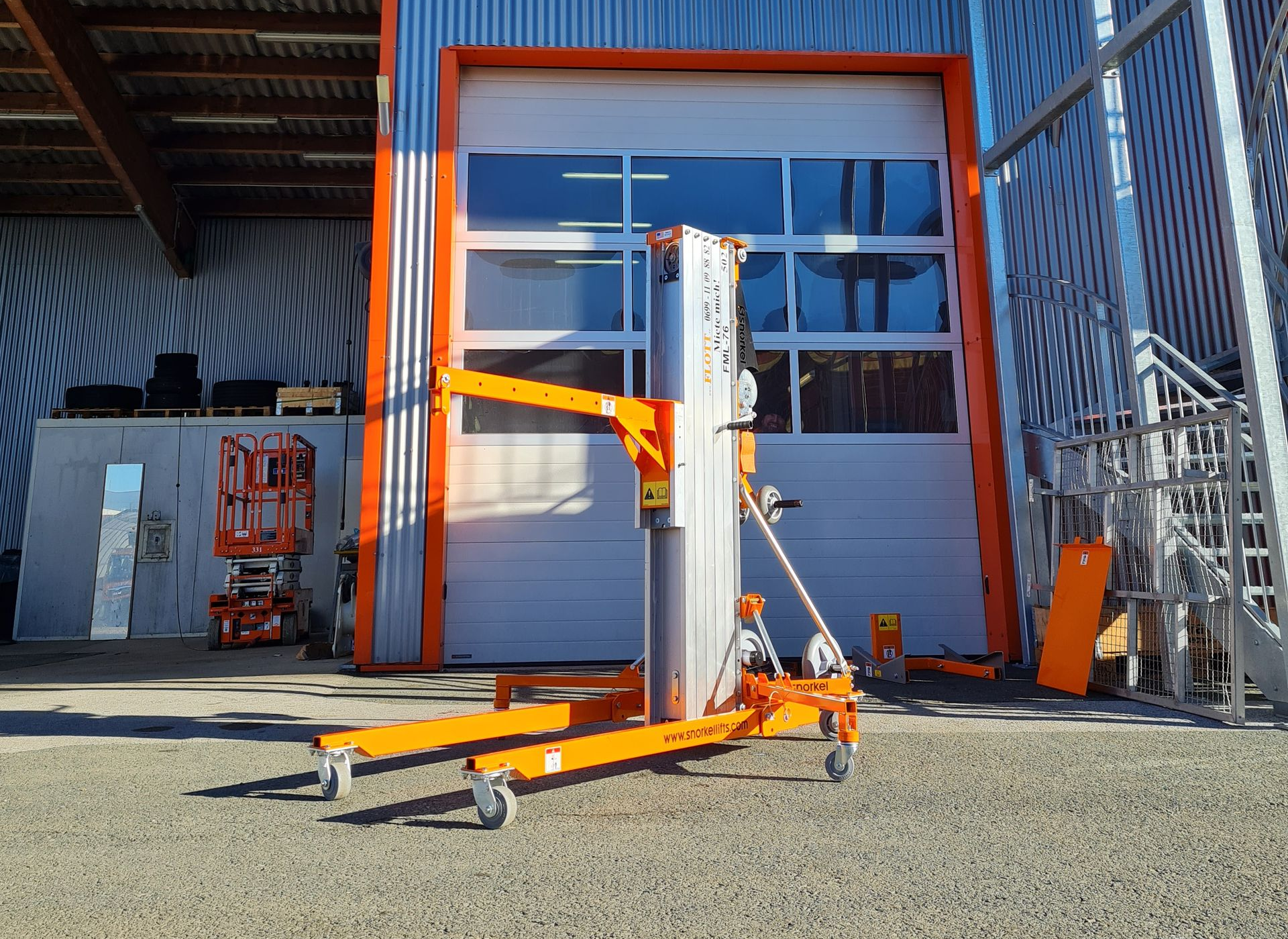 Orangefarbener Materiallift vor einem weißen Garagentor mit orangefarbenem Rahmen; im Freien.