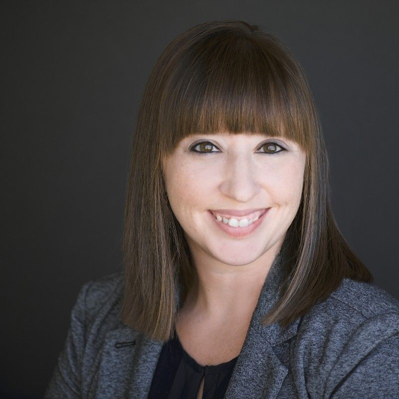 A woman in a gray jacket is smiling for the camera.
