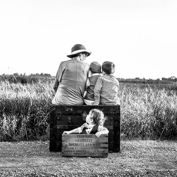 A woman and three children are sitting on a wooden box in a field.