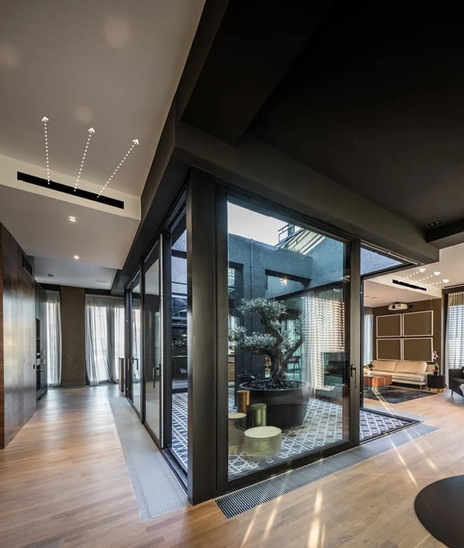 Cortile interno moderno con pareti in vetro, pavimenti in legno e illuminazione contemporanea.
