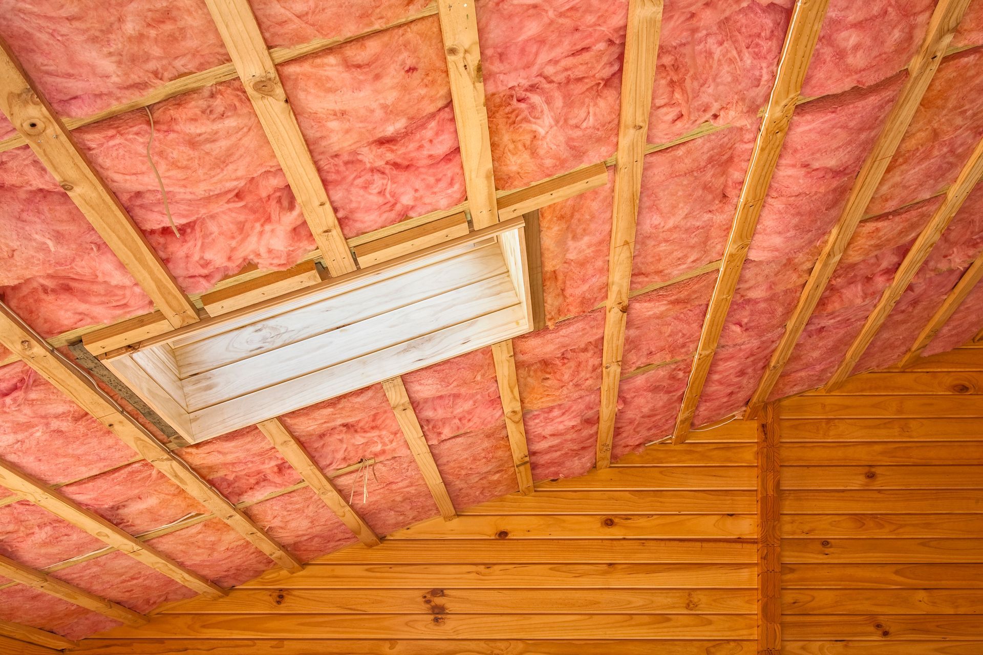 Pink fiberglass insulation installed in a wooden ceiling with exposed framing.