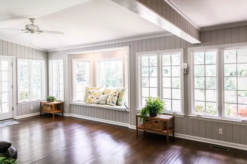 Spacious sunroom with dark wood floors, white-framed windows, built-in window seat with floral pillows