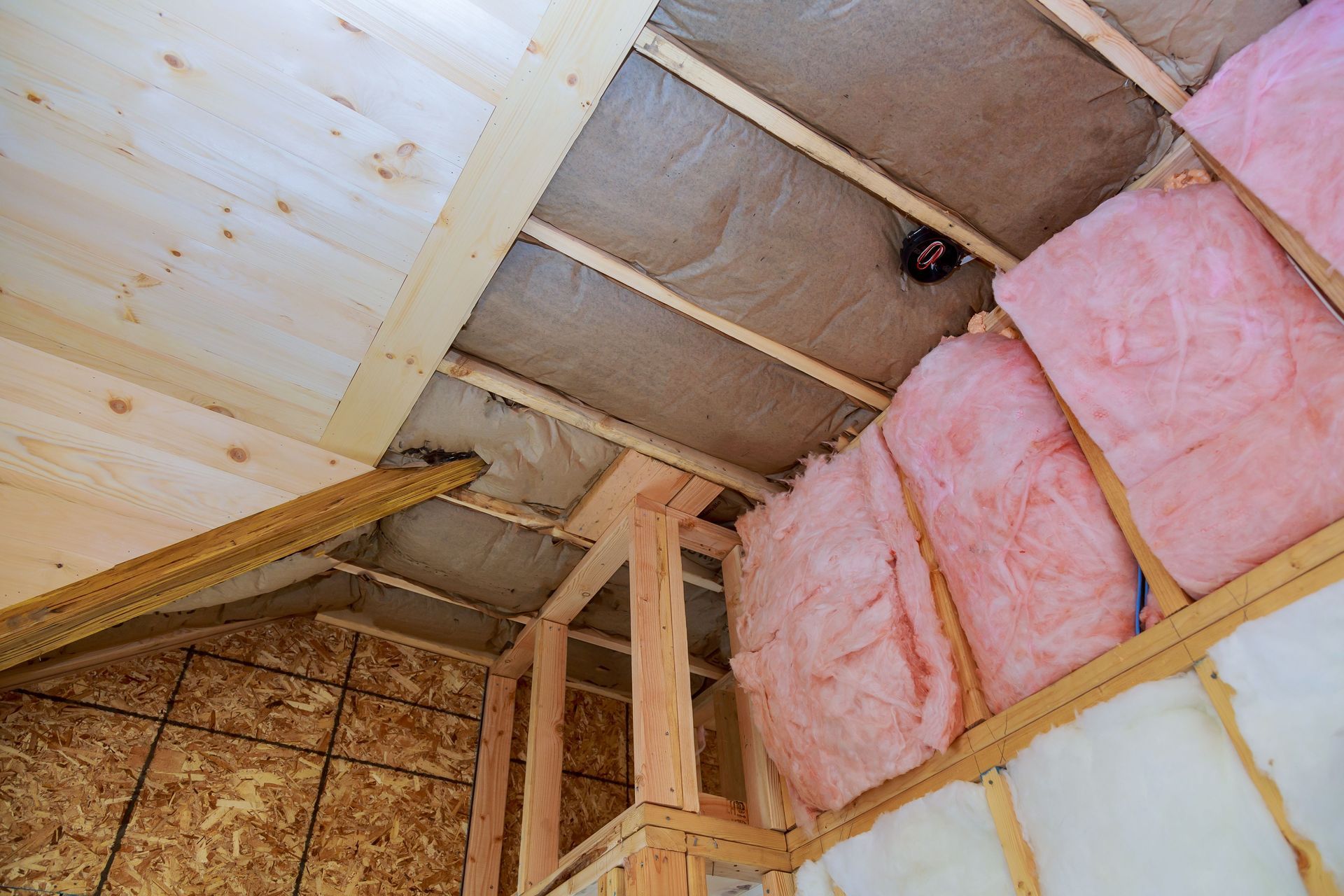 Unfinished attic space with exposed studs and pink insulation installed between beams.