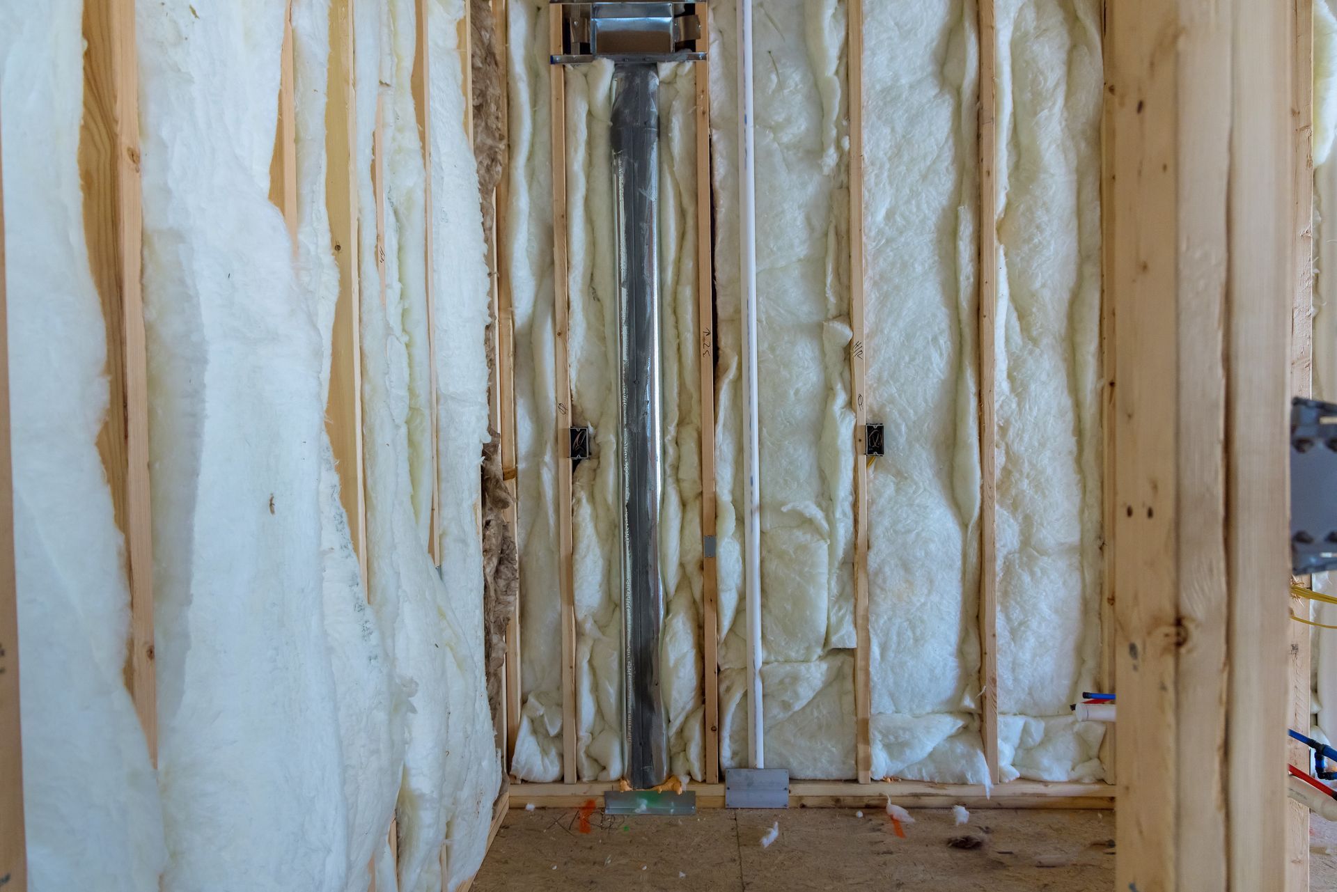Wooden studs with spray foam insulation, plumbing pipes, and metal ductwork. Interior framing of a building.