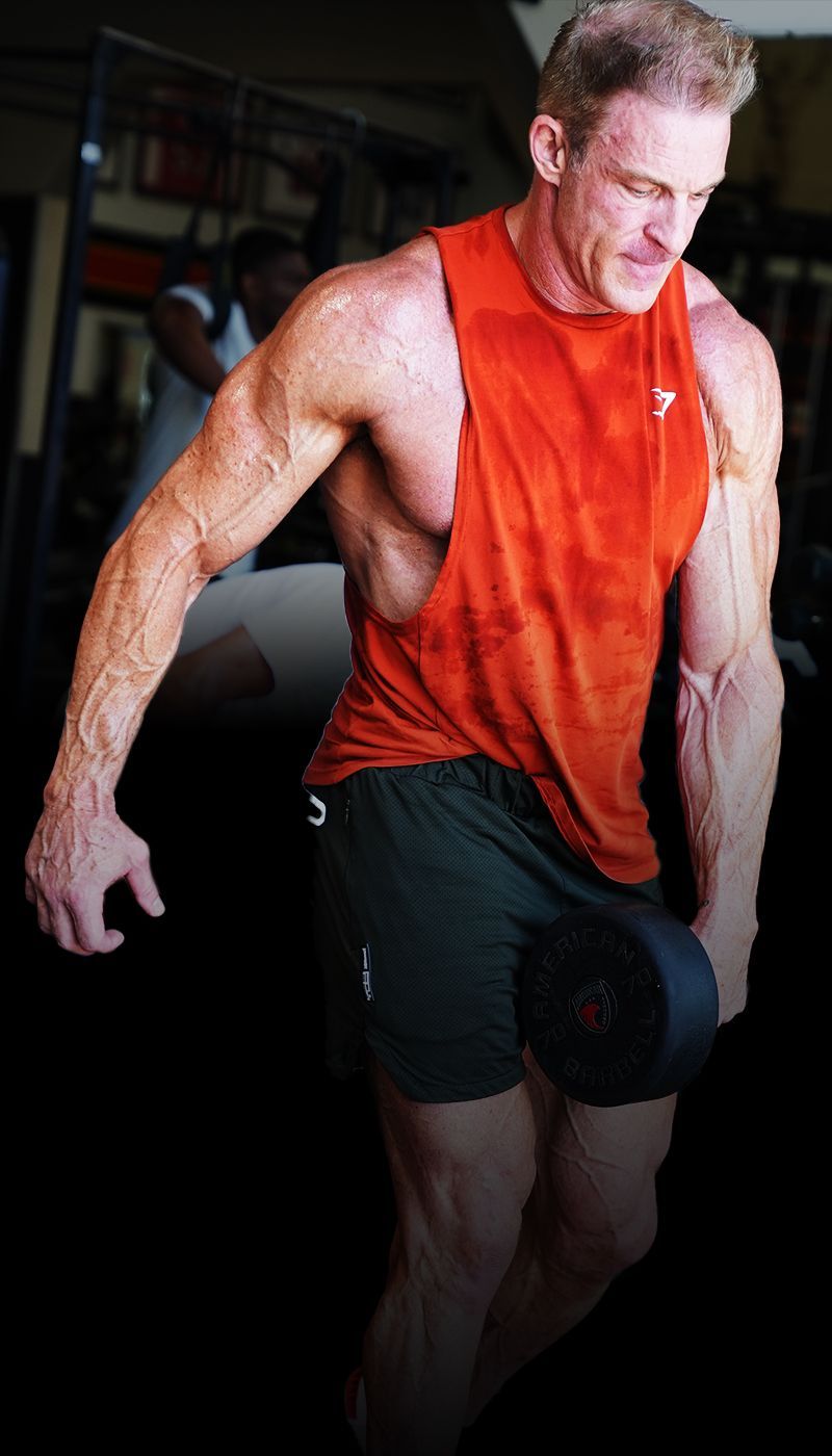 Ron Matthews in an orange tank top is lifting a dumbbell