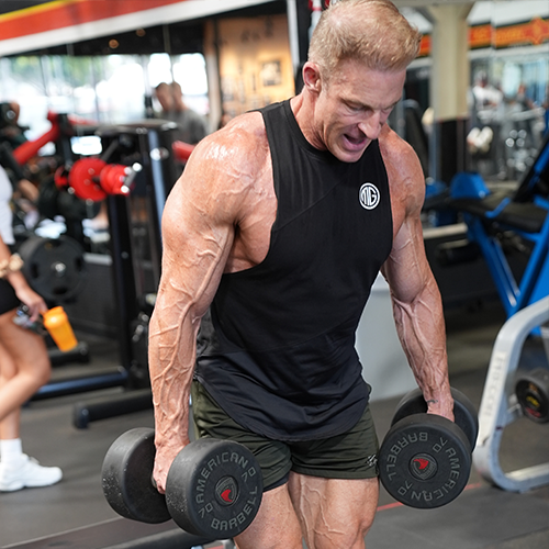 Ron Matthews is lifting two dumbbells in a gym.
