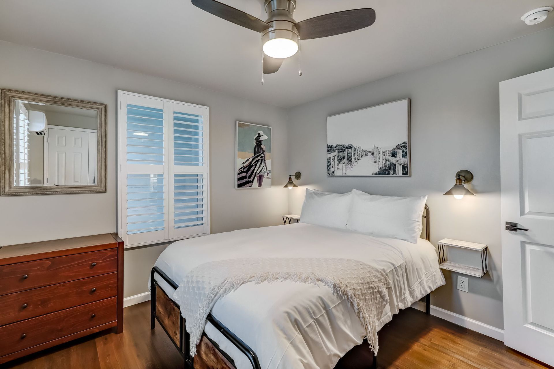 A bedroom with a queen size bed, air conditioning, ceiling fan and a dresser. 