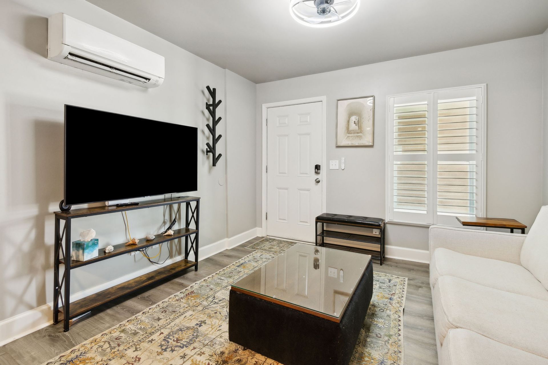 Living room view with smart TV, ottoman and a wall clothes hanger