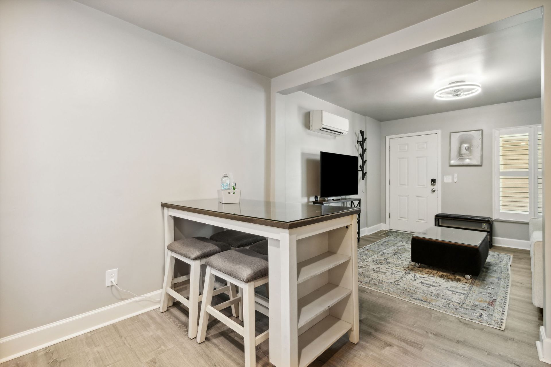 dining room and living room area with dining table, smart flat TV, ottoman and a mini split air conditioning unit on the wall