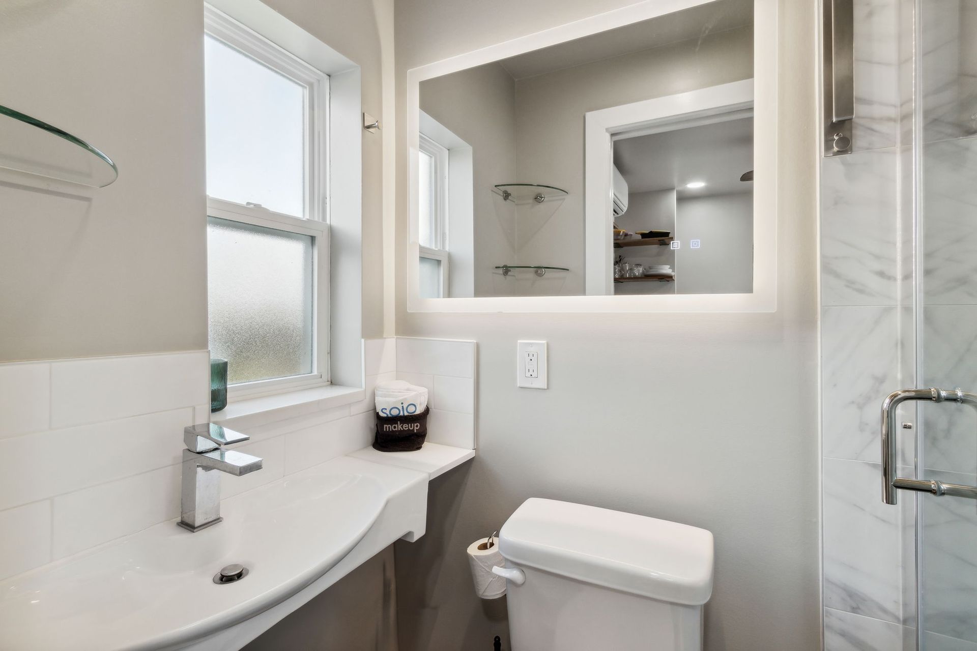 A bathroom with a toilet , sink , mirror and window.