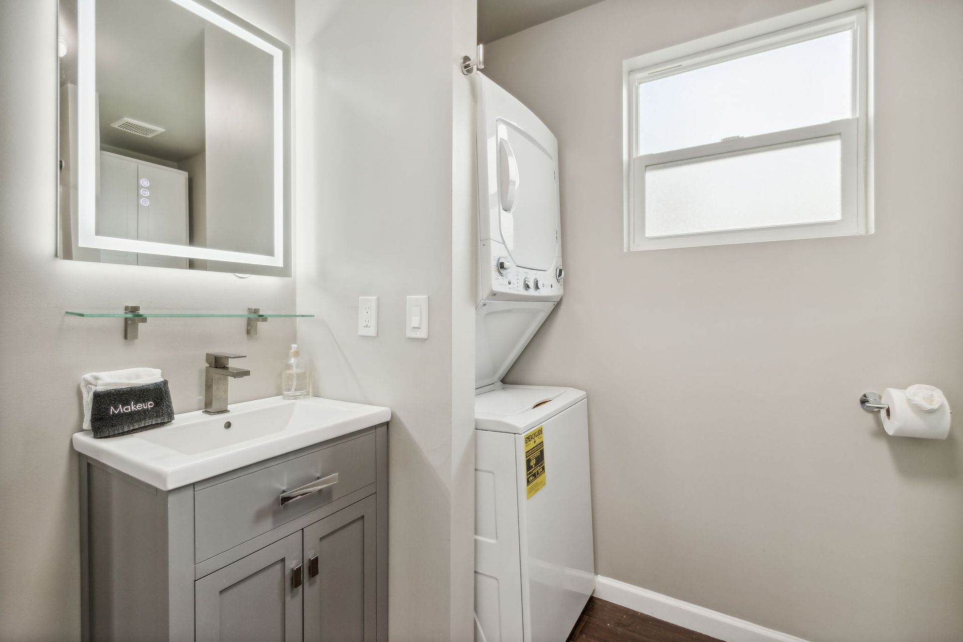 Bathroom vanity view with LED lit mirror and a washer/dryer combo in the back