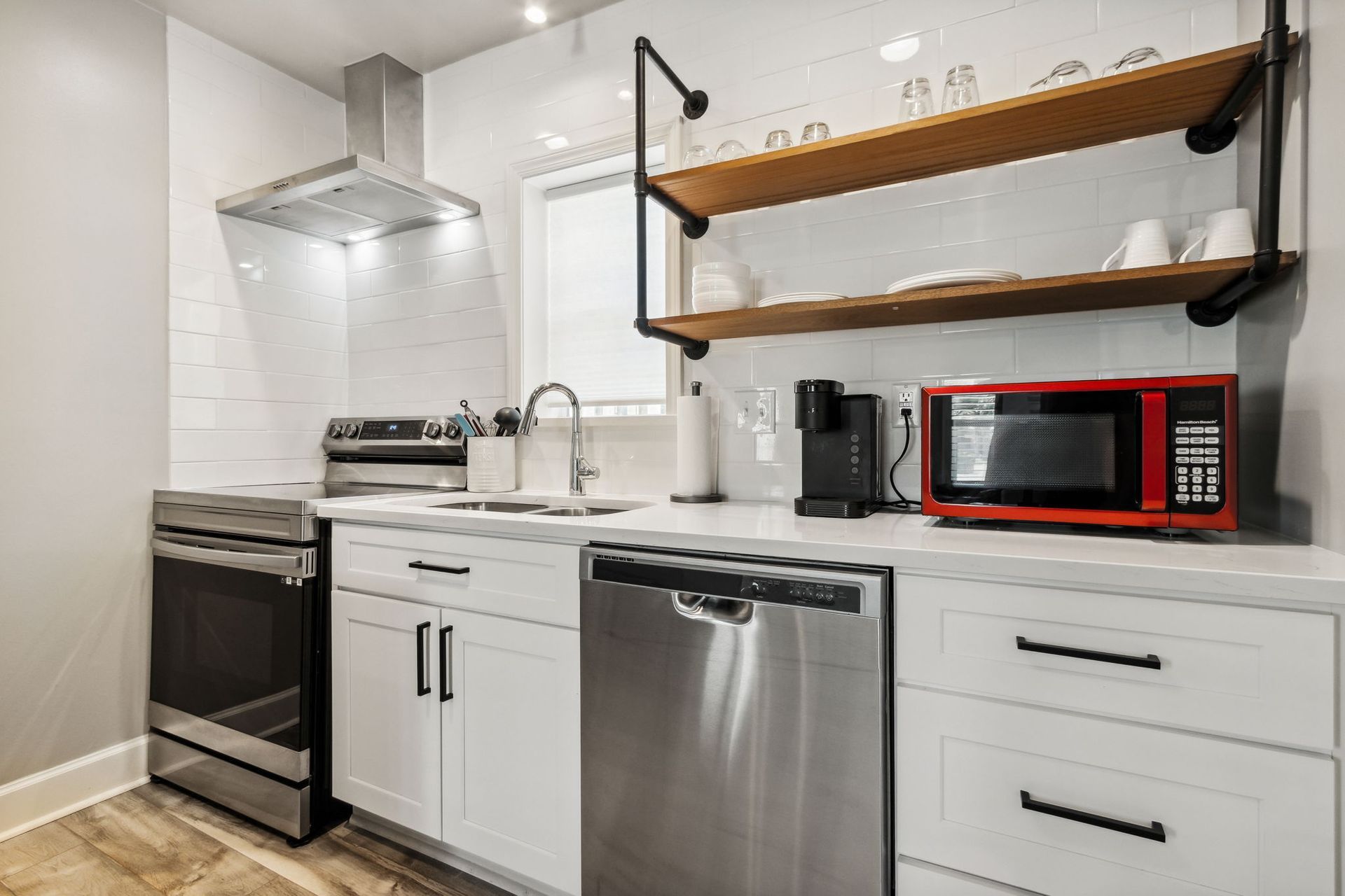 A kitchen with white cabinets, african mahogany shelving, stainless steel appliances, large pantry, and a red microwave.