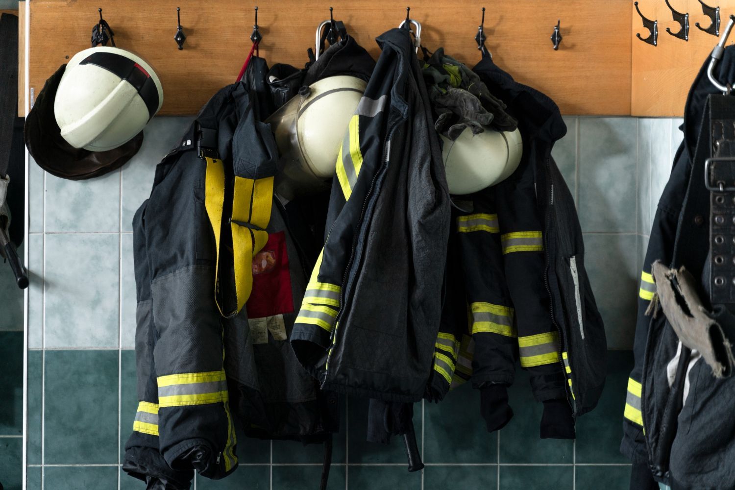 Equipo de bombero colgado en ganchos en una habitación embaldosada.