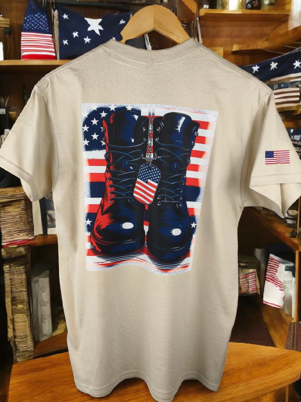 Camiseta beige con el dibujo de unas botas oscuras sobre una bandera estadounidense, colgada en una tienda rústica.