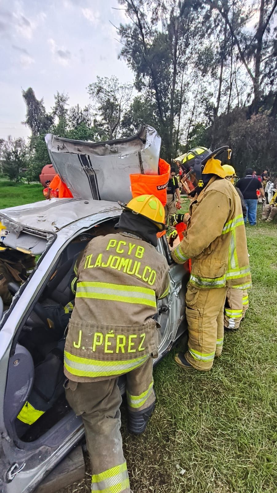 Bomberos con trajes realizan labores de rescate en un accidente de tráfico en una zona cubierta de hierba